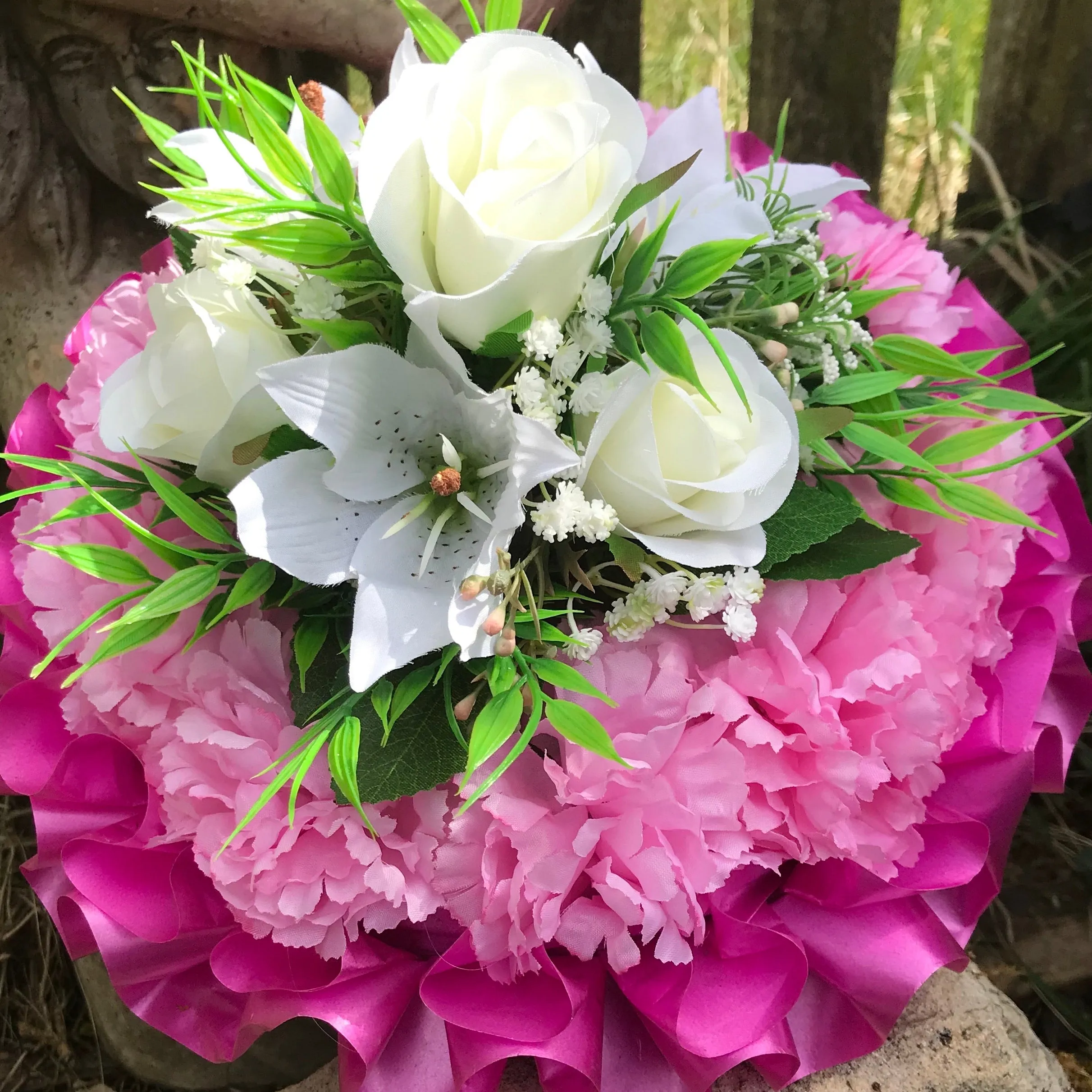 a funeral posy of artificial silk roses and lilies in shades of pink and white